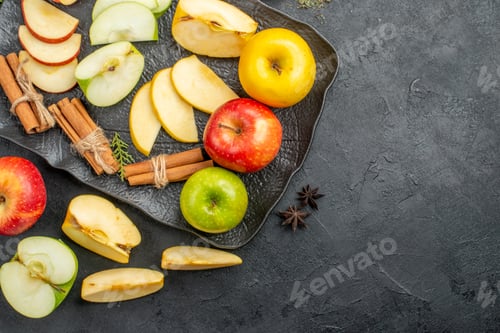 Preview: Above view of green yellow and red sliced and whole fresh apples on a black tray and cinnamon limes
