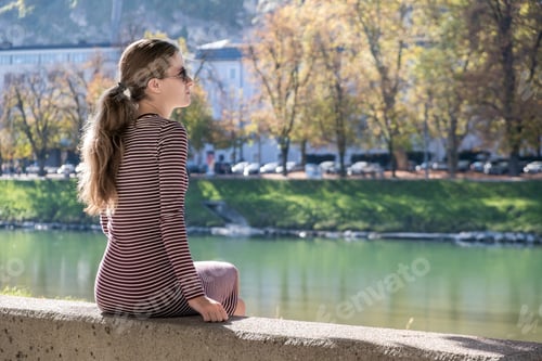 Preview: Young woman in a casual dress and sunglasses resting outdoors on a warm autumn day