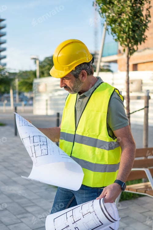 Preview: Male architect reviewing blueprints at construction site