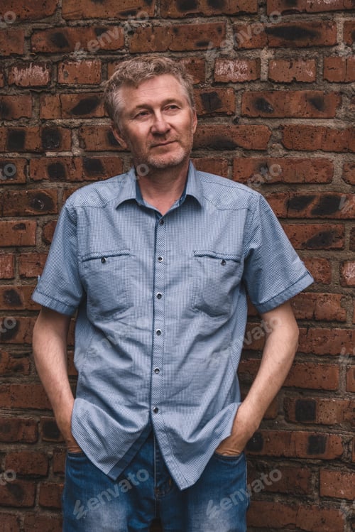 Preview: A candid portrait of a handsome, smiling, unshaven middle-aged man against a brick wall. Vertical.