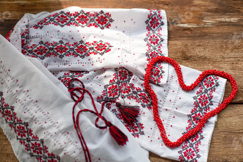 Preview: Ukrainian clothes embroidered white shirt. Red and black threads on a wooden background. Vyshyvanka
