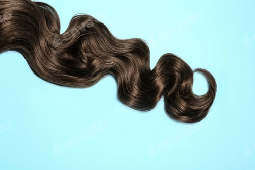 Preview: Lock of brown wavy hair on color background, top view