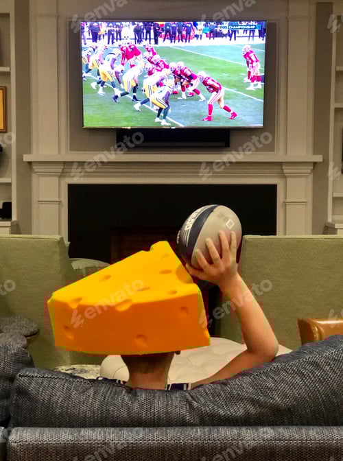Preview: Child football fan watching football at home holding football wearing Green Bay packers cheese head