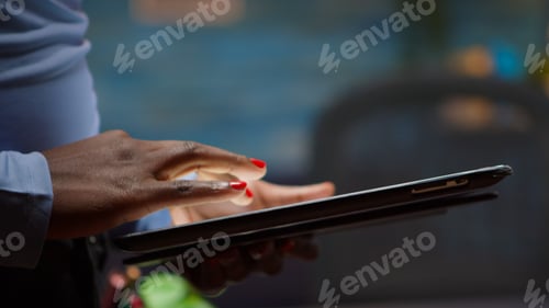 Preview: African employee using tablet standing in living room late