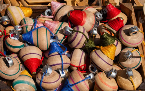 Preview: Closeup of wooden humming tops with threads in a box under the sunlight
