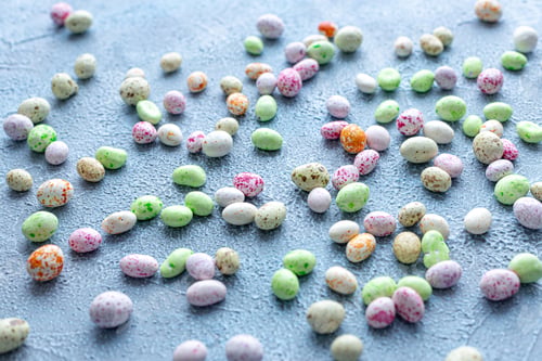 Preview: Candy, glazed chocolate Easter eggs sprinkled on a blue textured background.