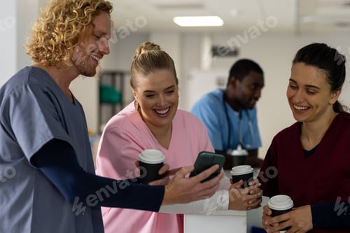 Preview: Happy diverse doctors drinking coffee and using smartphone at reception desk at hospital