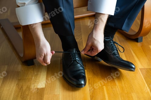 Preview: Man ties up the shoelaces of his black shoes.