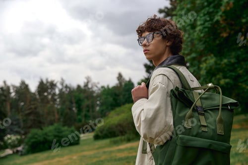Preview: Young handsome student enjoys a peaceful outdoor stroll in nature while carrying his backpack