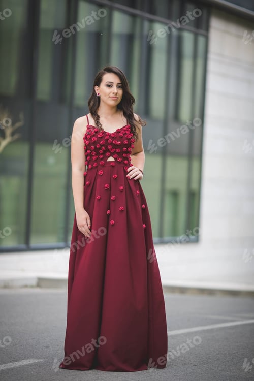Preview: Vertical shot of an elegant caucasian female in a red evening dress with small roses