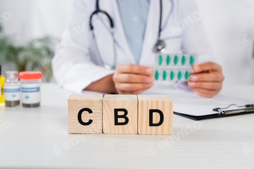 Preview: wooden cubes with cbd lettering near doctor holding blister pack with capsules on blurred background