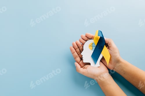 Preview: Hands holding a head with puzzle pieces and a ribbon. Celebrating Down Syndrome Day