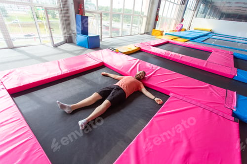 Preview: Fitness, fun, leisure and sport activity concept - Man lying on a trampoline indoors, top view