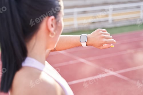 Preview: Young fitness woman looking at her smart watch while taking a break from sports training.