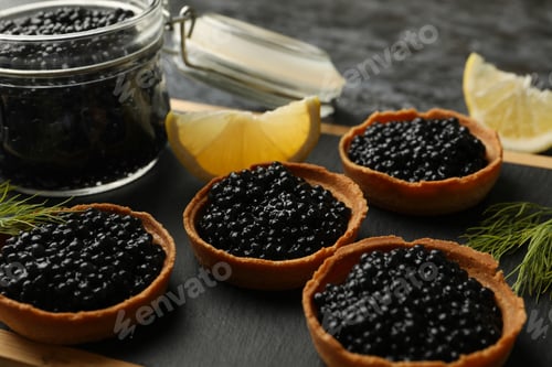 Preview: Board with tartlets and jar with caviar on black smokey background, close up
