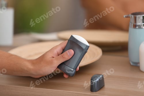 Preview: Young man holding deodorant over table in bathroom, closeup