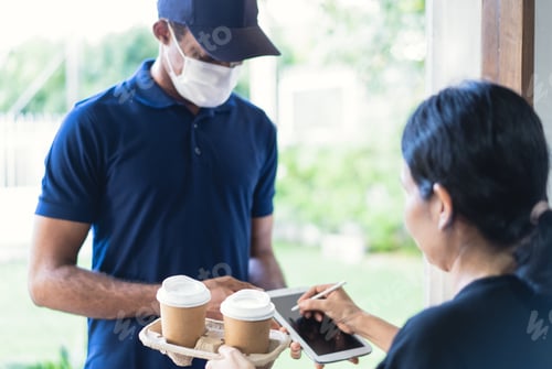 Preview: African American delivery man delivers takeaway coffee and holds a tablet for customers signature