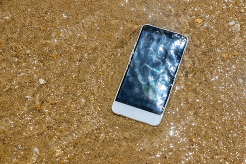 Preview: Broken crashed smartphone is lying in the water in the sandy beach