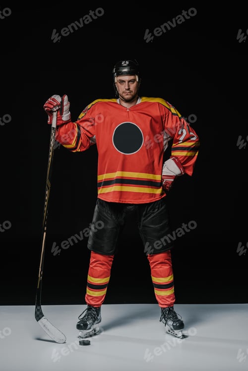 Preview: full length view of professional ice hockey player standing with hand on waist and looking at camera
