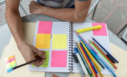 Preview: A student writing in a notebook and making notes on post its