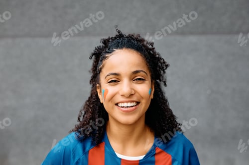 Preview: Happy black female soccer fan looking at camera.