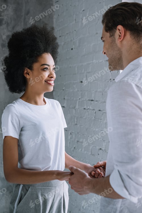 Preview: Multiracial couple holding hands by light wall