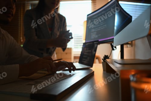 Preview: Cropped shot of developers brainstorming, programming code on computer screen at dark office