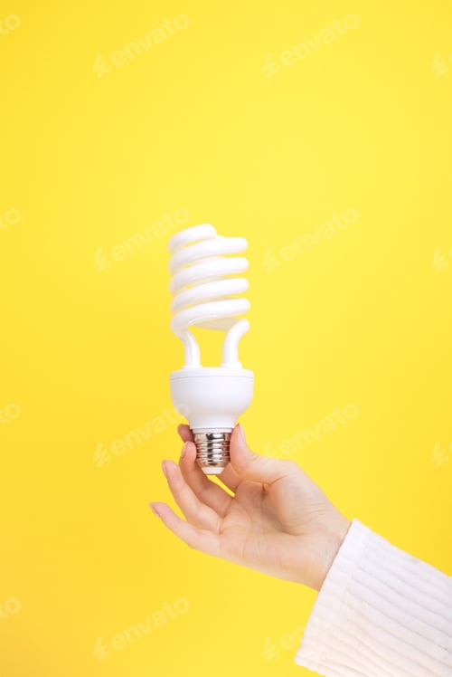 Preview: Female hand holds an Fluorescent Lightbulb on a yellow background.
