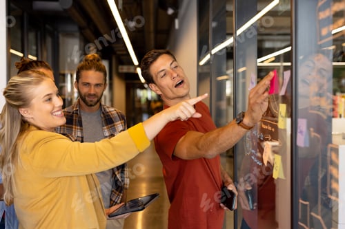 Preview: Happy diverse creative colleagues in discussion brainstorming making notes on glass wall in office