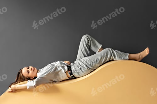 Preview: Portrait of a young woman lying on a chaise lounge chair in the shape of a wave on a blue background