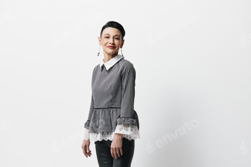 Preview: Fashionable Asian woman in black leather pants and gray blouse standing by white wall