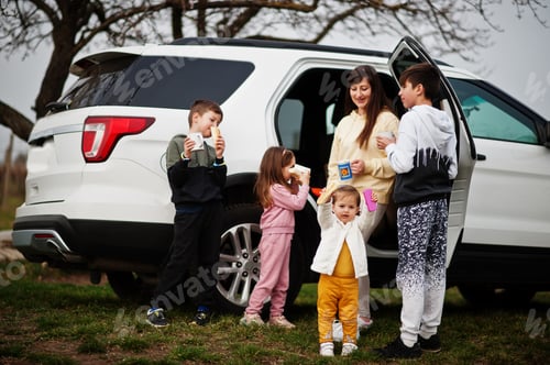 Preview: Mother with kids drink tea outdoor near white suv car.
