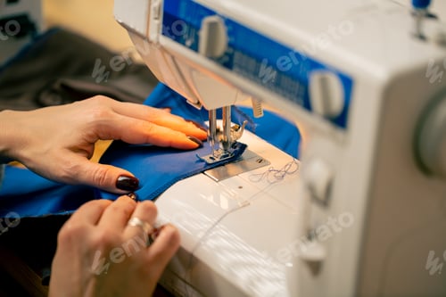 Preview: close-up in a sewing workshop on a machine the seamstress master makes cut on a blue fabric