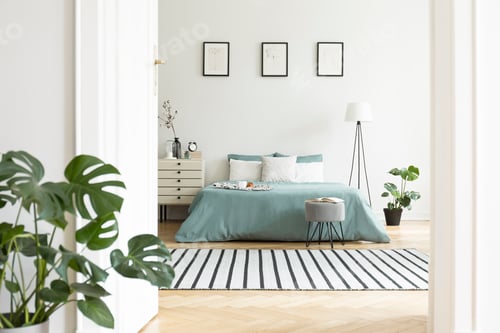 Preview: Posters above green bed in white bedroom interior with plants an