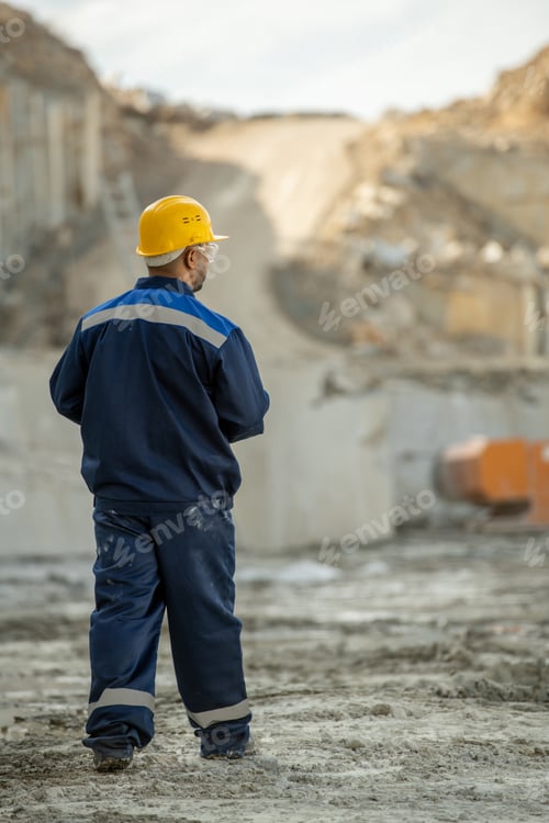Preview: Rear view of contemporary quarry worker in uniform and hardhat