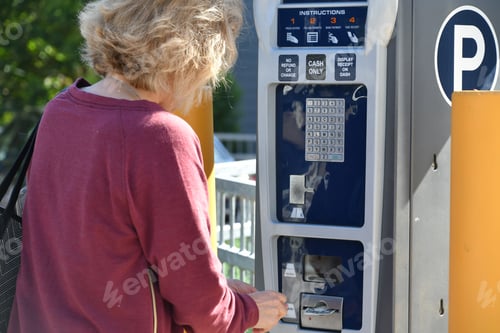 Preview: A woman putting money dollar bills into a parking kiosk to pay for parking in a lot in the city. -