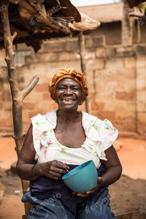 Preview: Elderly woman smiling with a blue bowl in her hands sitting outside her home