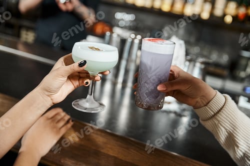 Preview: cropped view of multiethnic female colleagues holding delicious cocktails in bar after work