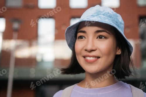 Preview: Smiling beautiful asian woman wearing casual clothing, stylish panama looking away on the street