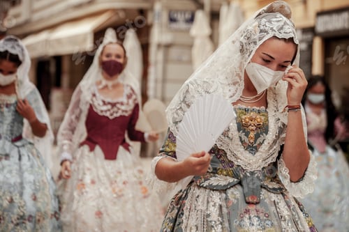 Preview: A girl dressed as a fallera parades while fanning herself and wiping her sweat in Valencia.