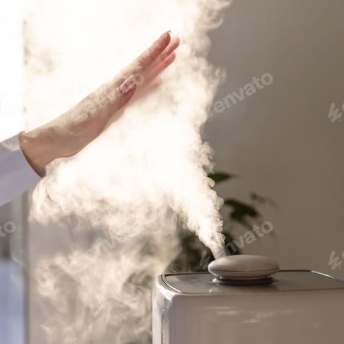 Preview: Woman holds hand over steam aroma oil diffuser on the table at home, steam from the air humidifier