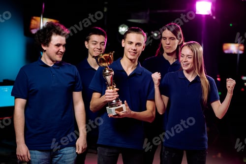 Preview: Young leader of cybersports team holding golden cup among his friends