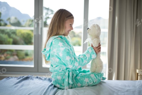 Preview: Smiling girl holding teddy bear on bed in bedroom