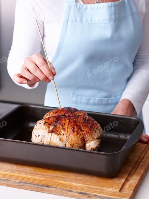 Preview: Person checking roasted chicken with a skewer