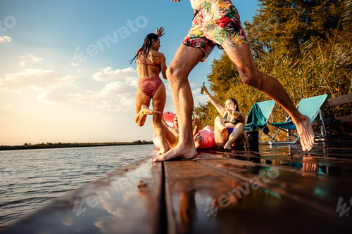Preview: Group of friends having fun drinking beer, enjoying a summer day swimming and jumping at the lake.