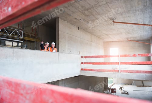 Preview: Two men wearing safety vests talking in building under construction