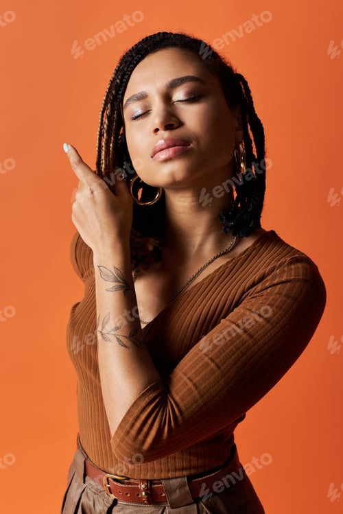 Preview: Stylish young woman poses confidently in a vibrant studio setting with orange backdrop