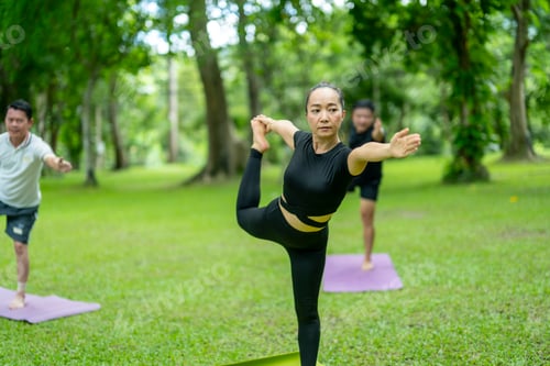 Preview: A woman is doing a yoga pose in a park with two other people