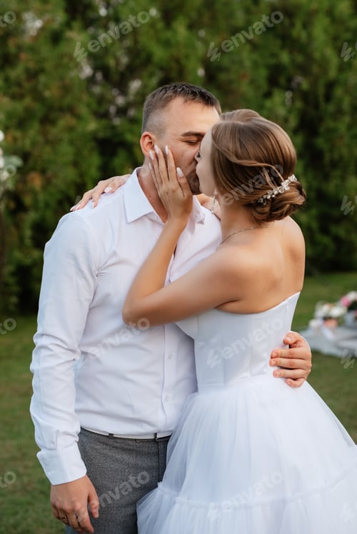 Preview: the first dance of the groom and bride in a short wedding dress on a green meadow