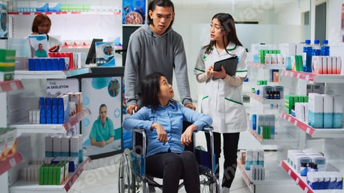 Preview: Pharmacy employee giving pills box to woman in wheelchair